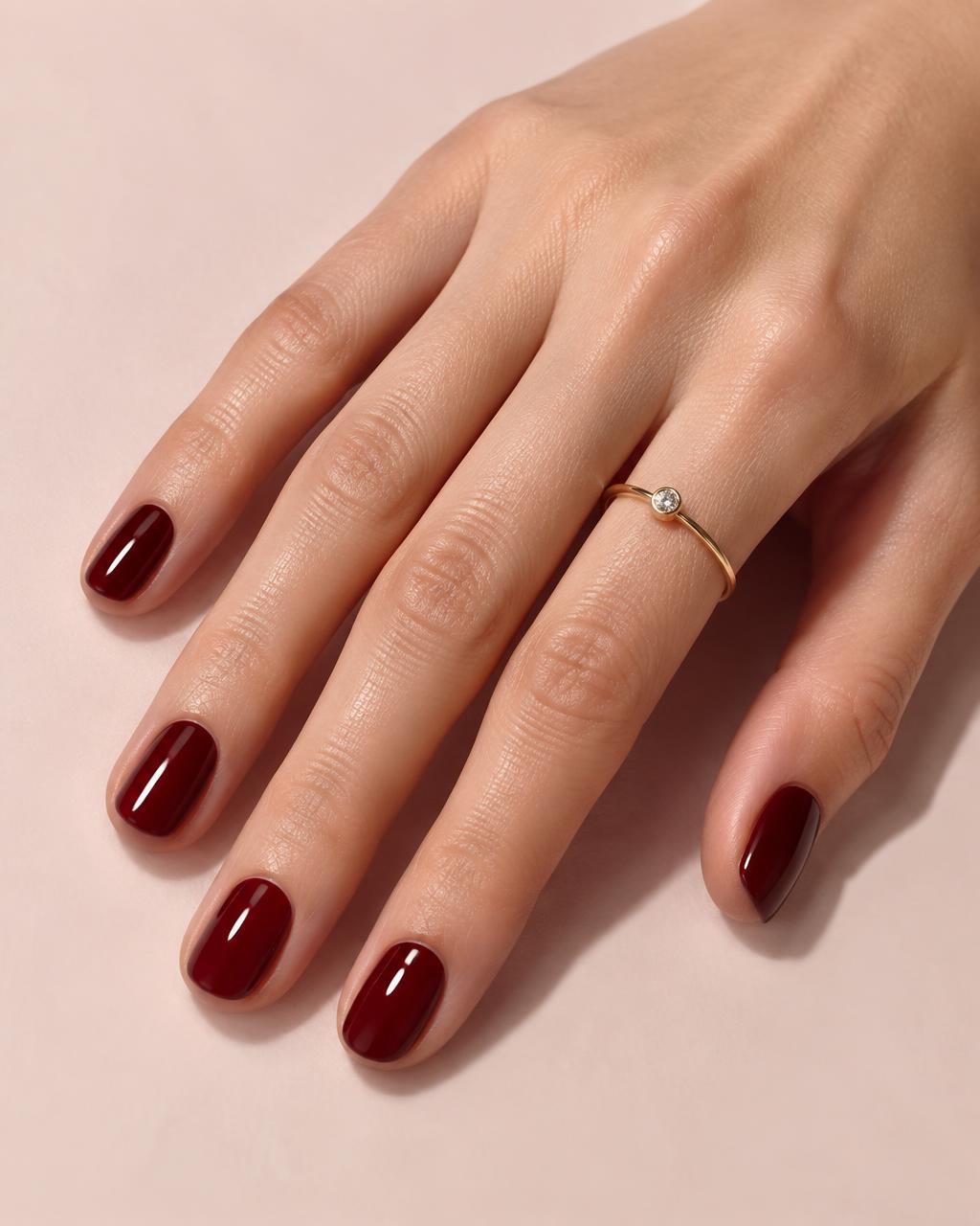 Mão com unhas curtas em esmalte vinho brilhante e um anel fino